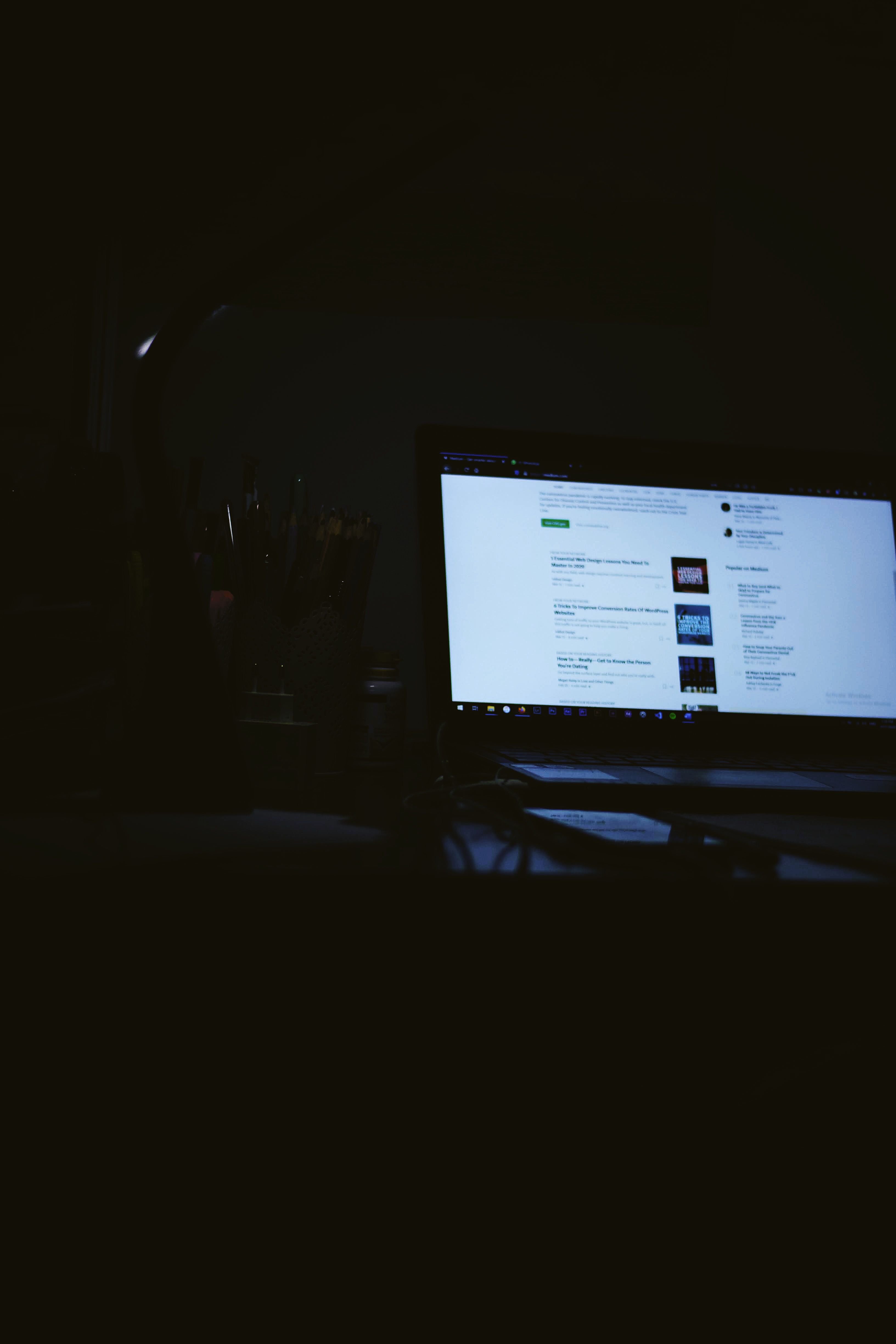 Laptop and monitors on a desk in a dim office with notebook workspace screen